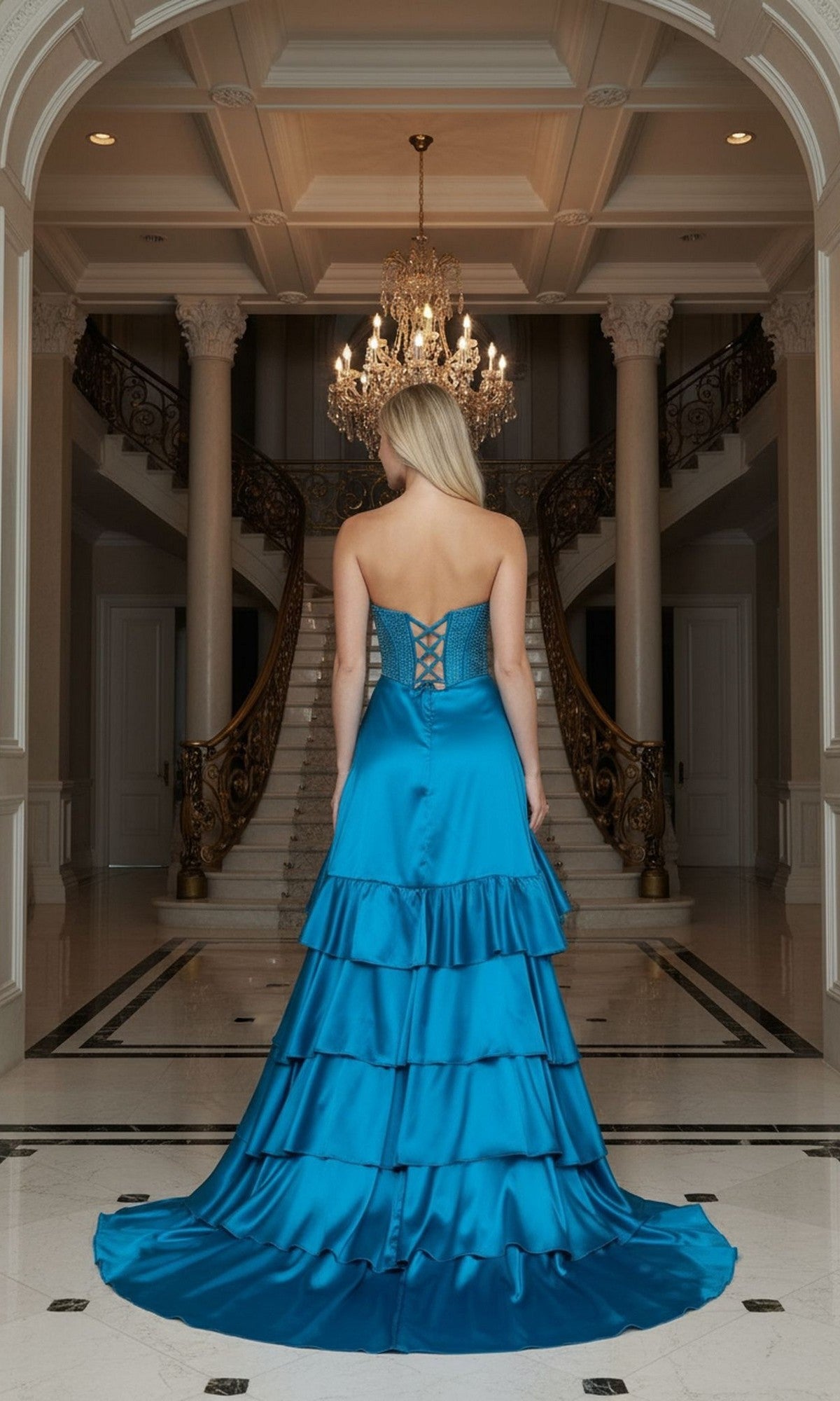 A woman in the Poly USA 25162 long prom dress with a strapless, embellished corset bodice stands facing away in an elegant foyer beneath a chandelier by a double staircase.